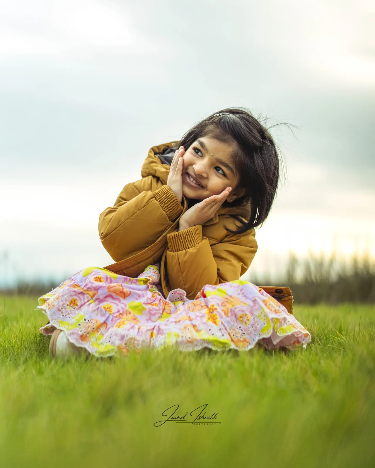 A little girl sitting in the grass at golden hour
