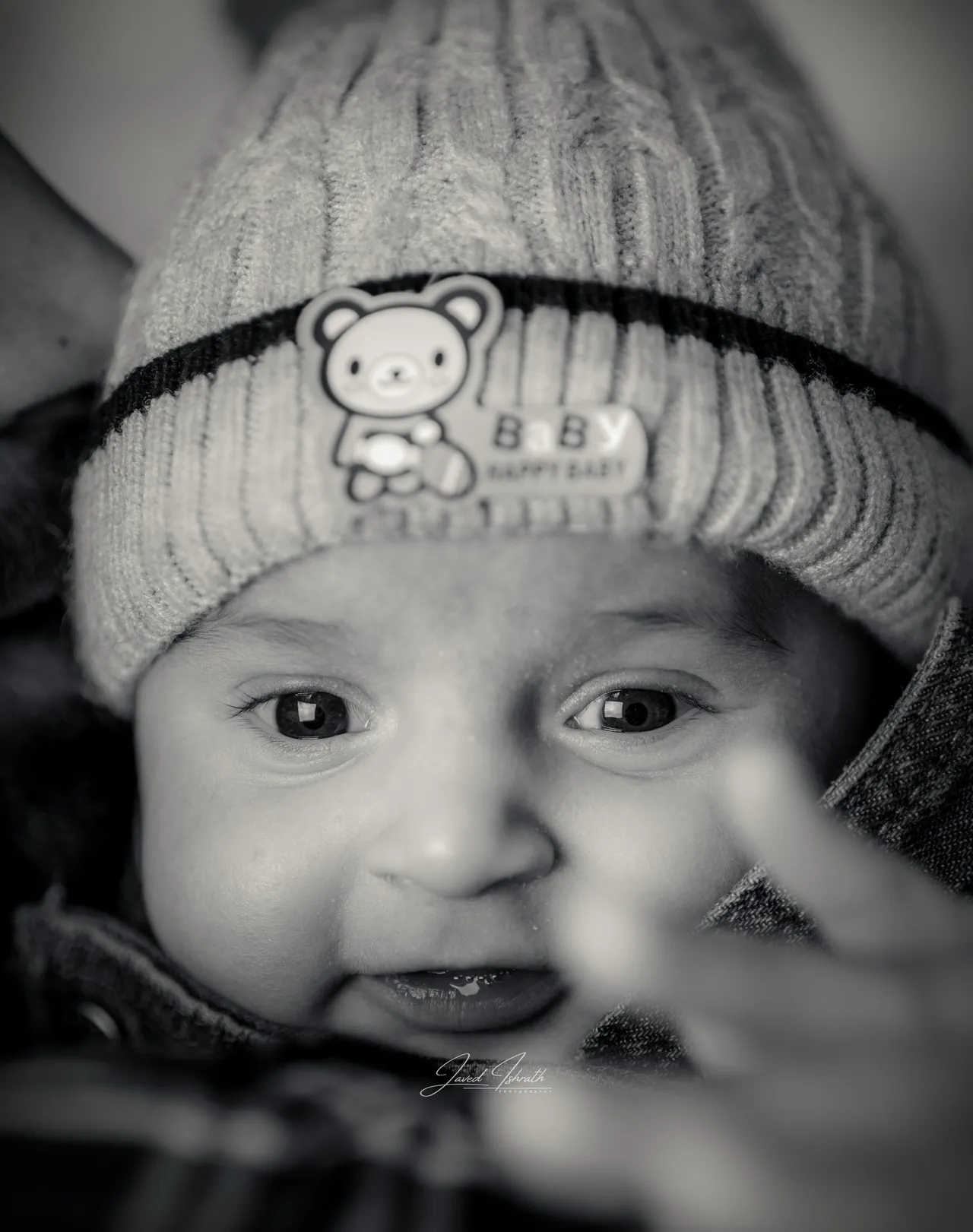 Black and white close-up of a smiling baby in a knitted hat