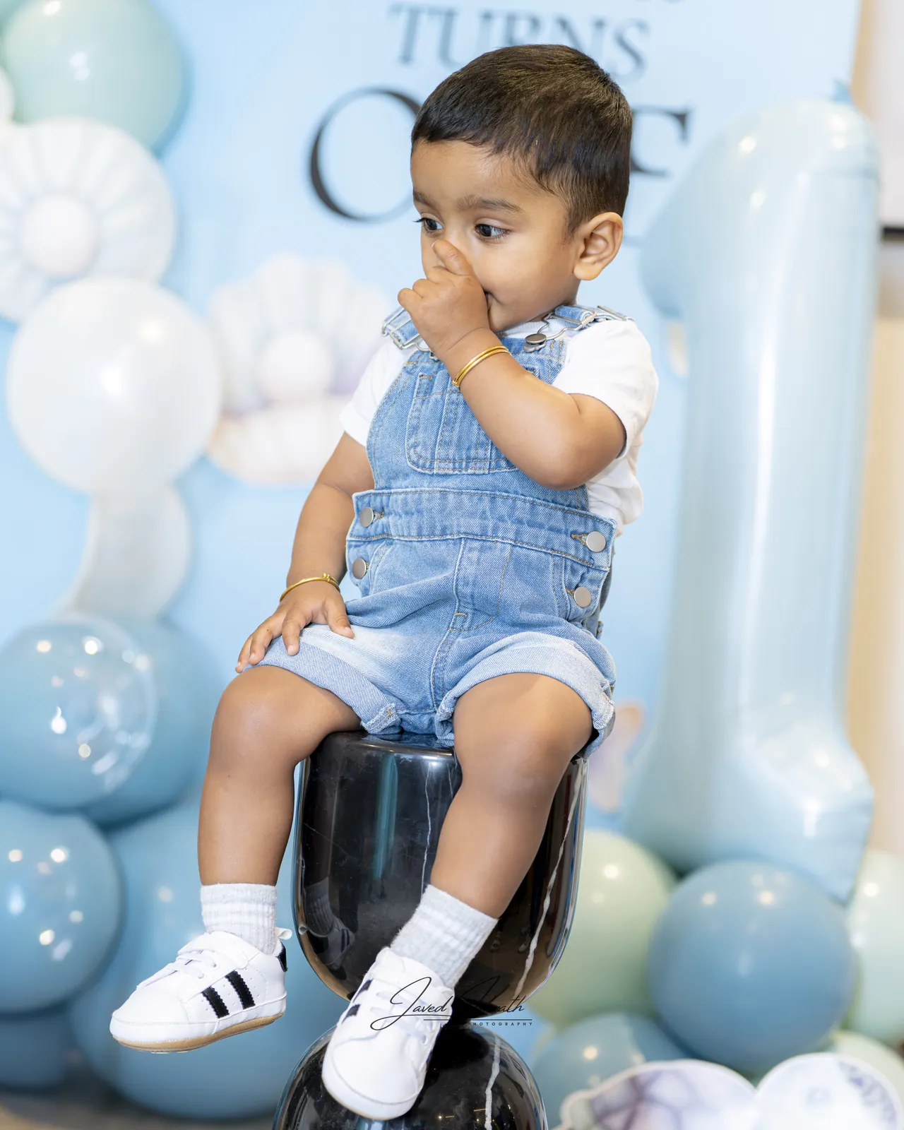 A toddler sitting on a stool in front of blue balloons